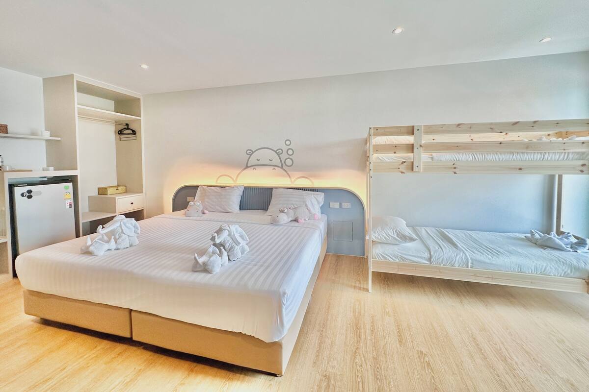 A modern hotel room with a large bed, a bunk bed, a small kitchenette, and a wardrobe.