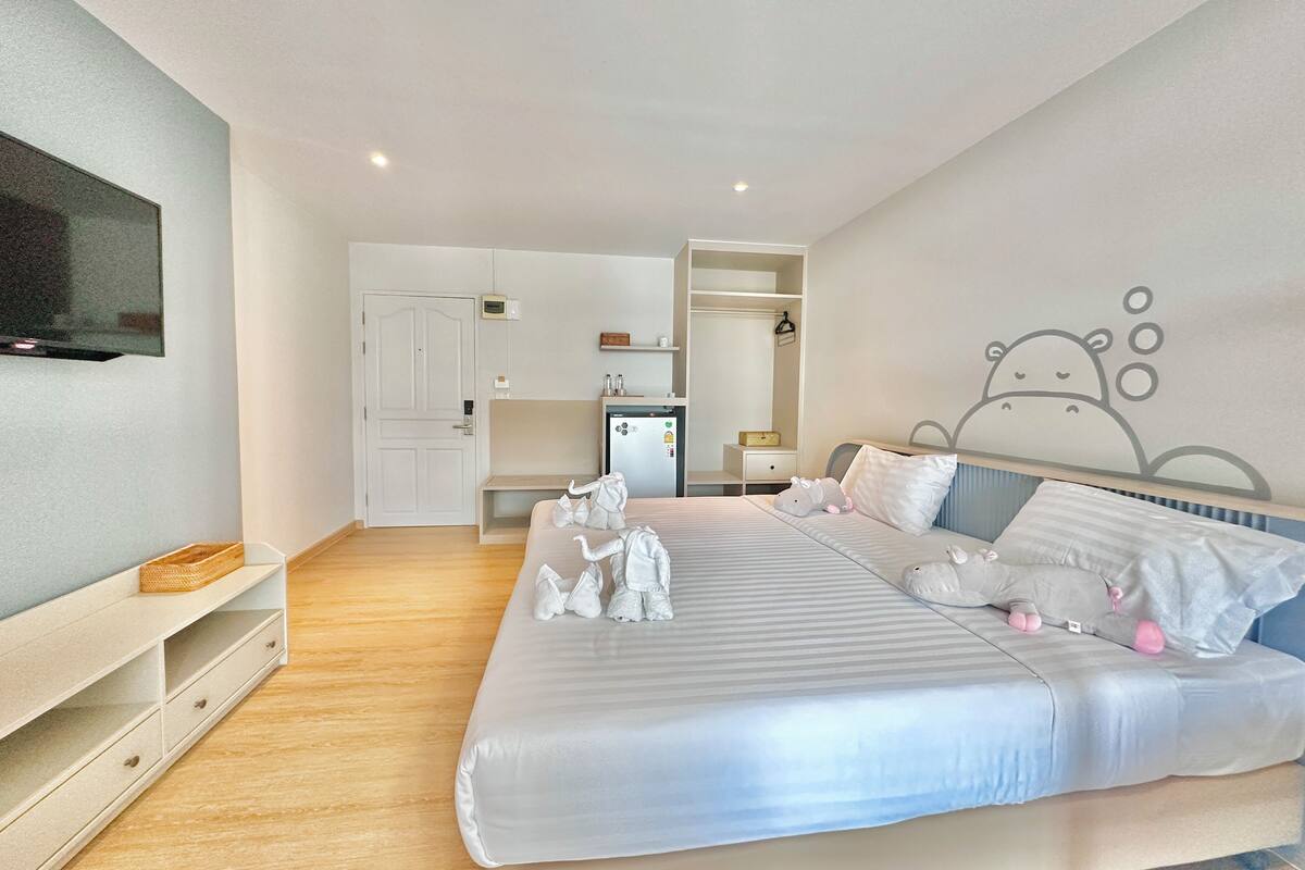 A modern bedroom with a large bed, a television, a wardrobe, and a small kitchenette.