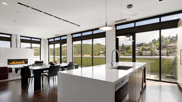 A modern kitchen with a large island, a built-in fireplace, and a view of a green hillside.