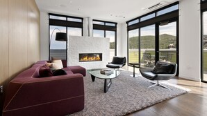 A modern living room with a fireplace, large windows, and a view of the outdoors.