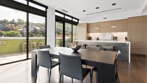 A modern kitchen with a large island, dark chairs, and a view of a residential area through large windows.