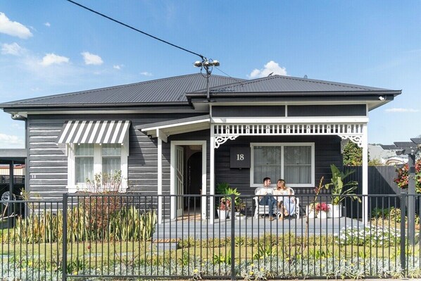A two-story house with a porch, number 18, and a small garden in front. - Maggie’s the Little Black Cottage - In the Heart of the Hunter Valley (Cessnock)