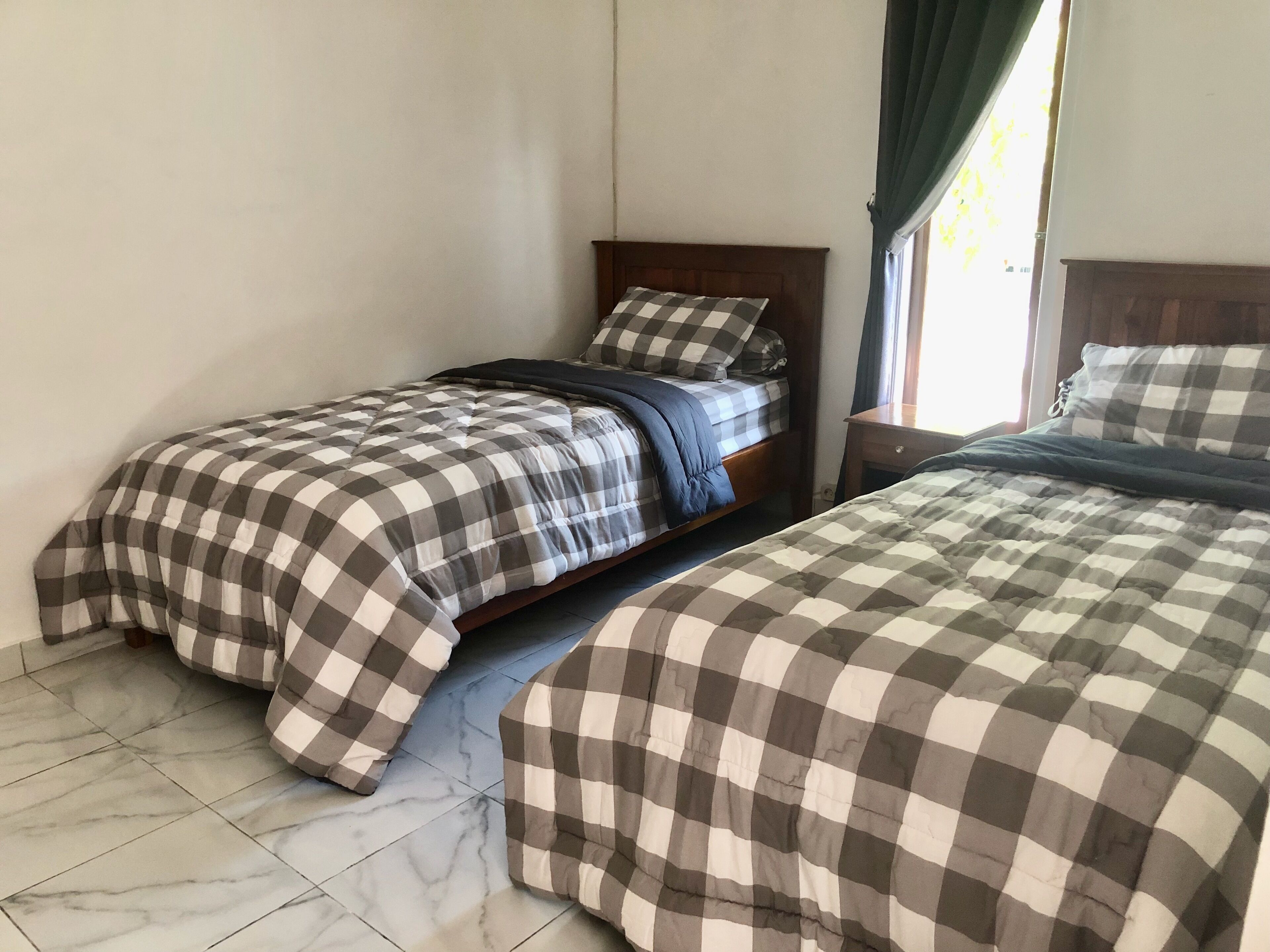 A bedroom with two beds, each with a checkered bedspread, a wooden headboard, and a nightstand with a lamp.