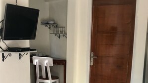 Un salon avec un canapé, un téléviseur fixé au mur, une porte en bois et une petite table sur laquelle est posée une plante.