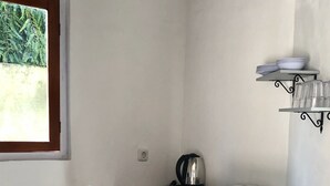 Un petit coin cuisine avec une table en bois, deux chaises blanches, une bouilloire et une étagère remplie de vaisselle.