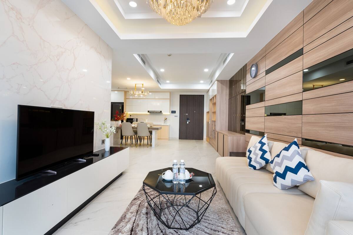Una sala de estar moderna con un televisor de pantalla plana, una mesa de centro con botellas de agua y un sofá con almohadones estampados.
