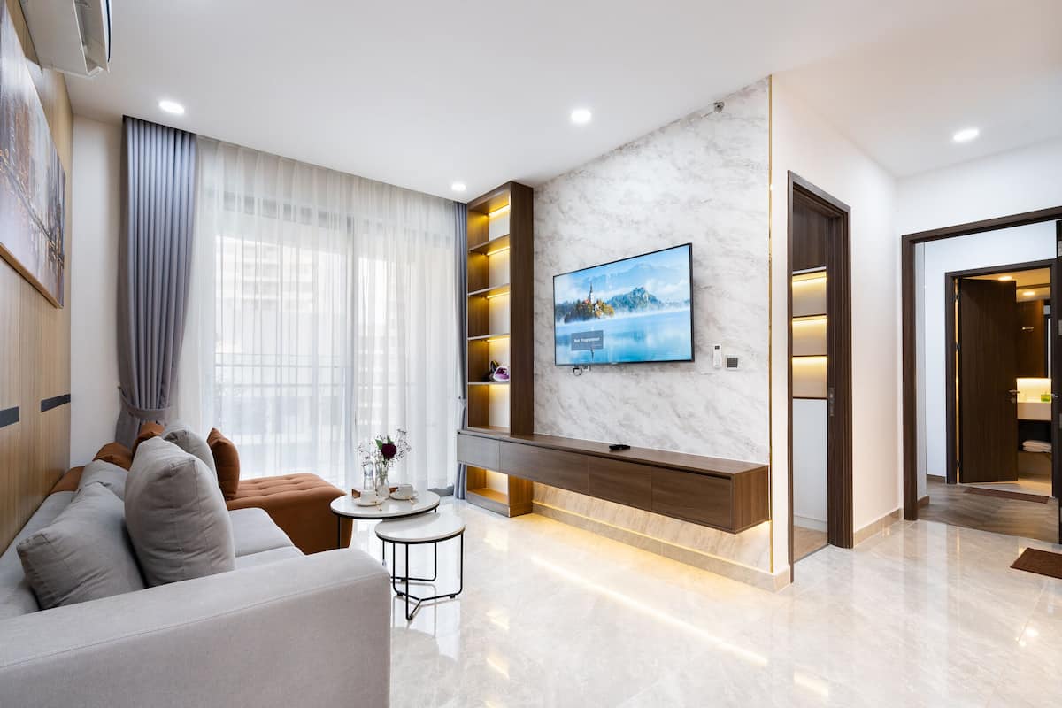 Una sala moderna con un sofá, una mesa de centro, un televisor montado en una pared de mármol y una estantería empotrada.