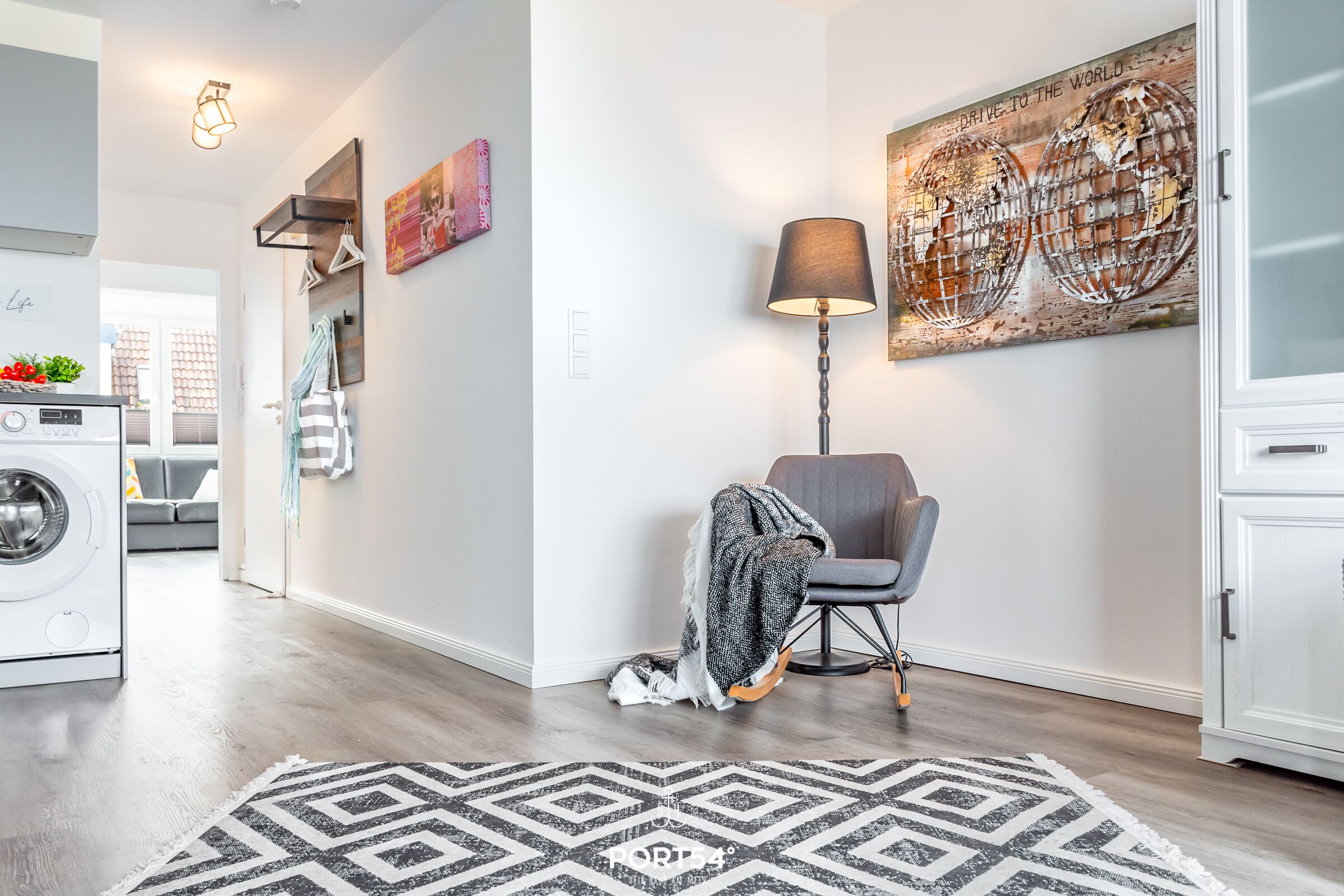 A modern living room with a geometric rug, a chair with a blanket, a lamp, and a wall art piece.