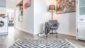 A modern living room with a geometric rug, a chair with a blanket, a lamp, and a wall art piece.