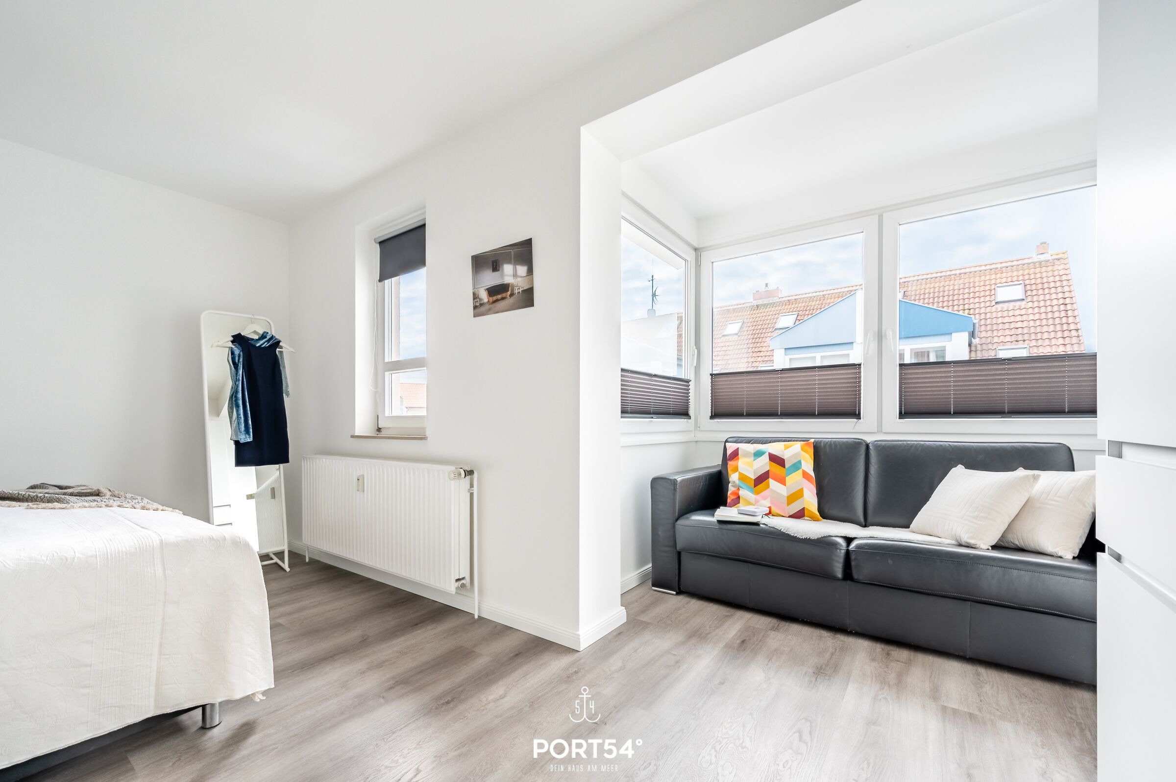 Ein modernes, helles Zimmer mit einem Bett, einem grauen Sofa und einer Heizung.