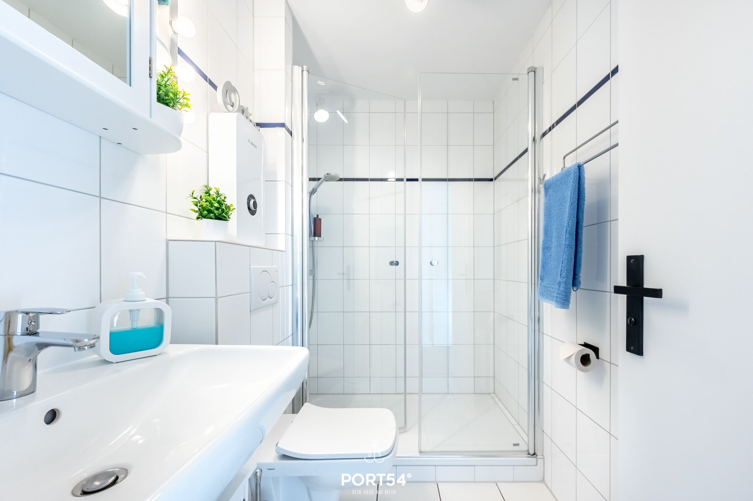 A modern bathroom with a white sink, a glass shower enclosure, and a blue towel hanging on a black towel rack.