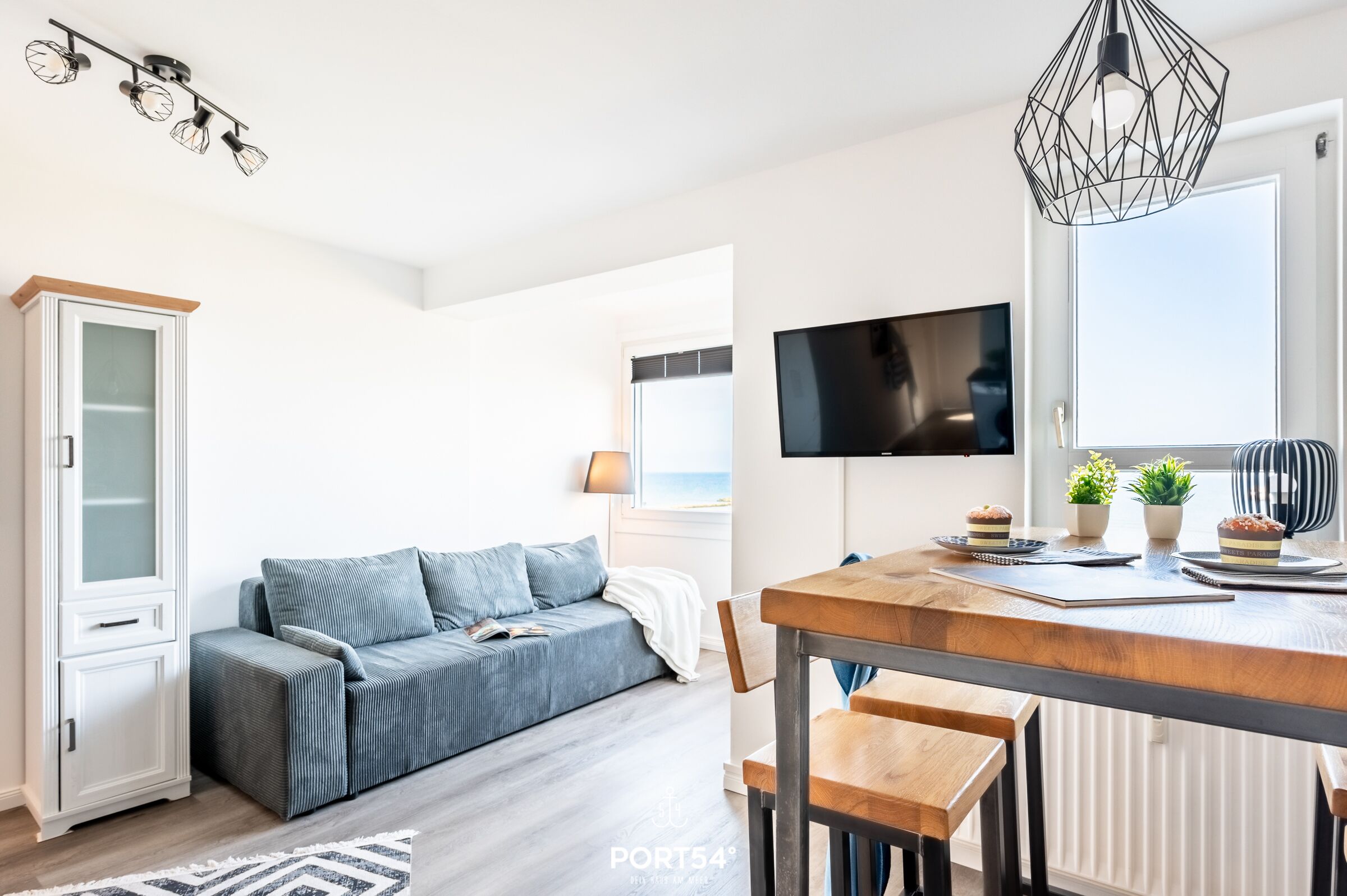 Een moderne woonkamer met een bank, een eettafel met stoelen, een aan de muur bevestigde televisie en een raam met uitzicht.