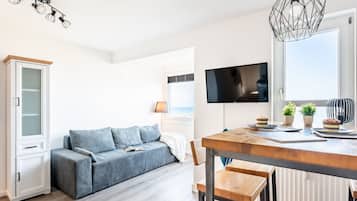 Een moderne woonkamer met een bank, een eettafel met stoelen, een aan de muur bevestigde televisie en een raam met uitzicht.