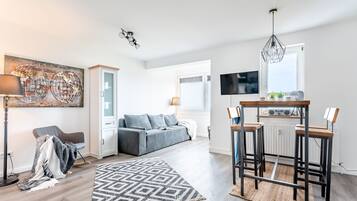 Un salon moderne avec un canapé gris, un tapis à motifs, une table basse et un téléviseur fixé au mur.