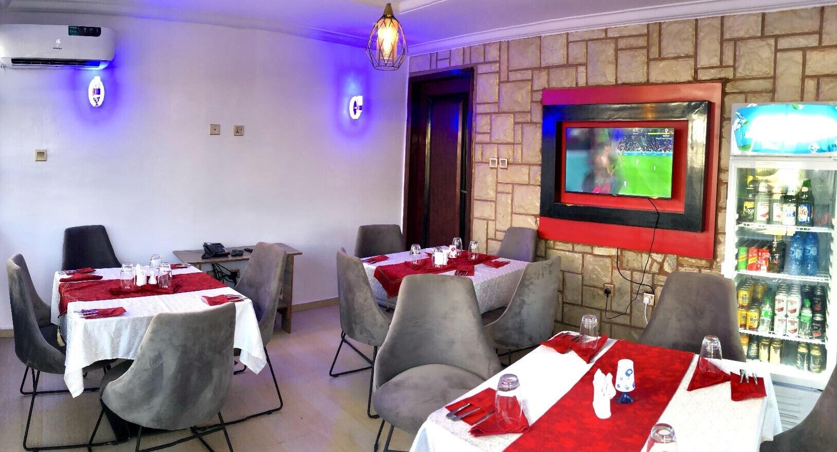 A restaurant with tables set for dining, a television mounted on the wall, and a beverage refrigerator.