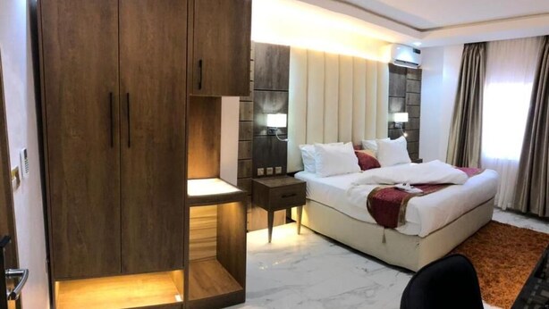 Ein Hotelzimmer mit großem Kleiderschrank, einem Bett mit weißer Bettwäsche, einem Nachttisch und Teppichboden.