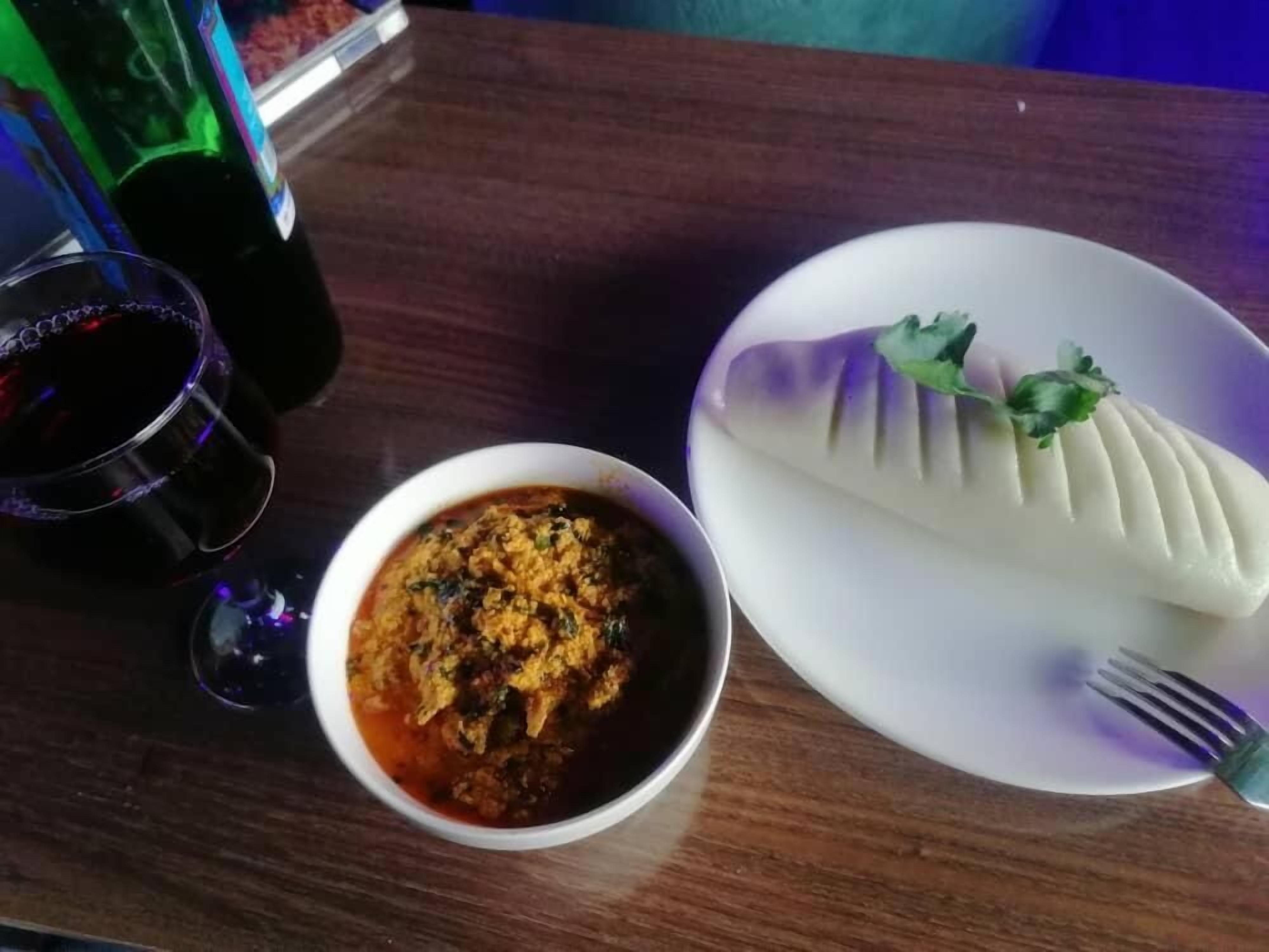 Una mesa con un plato de comida, un tazón de estofado y una copa de vino tinto.