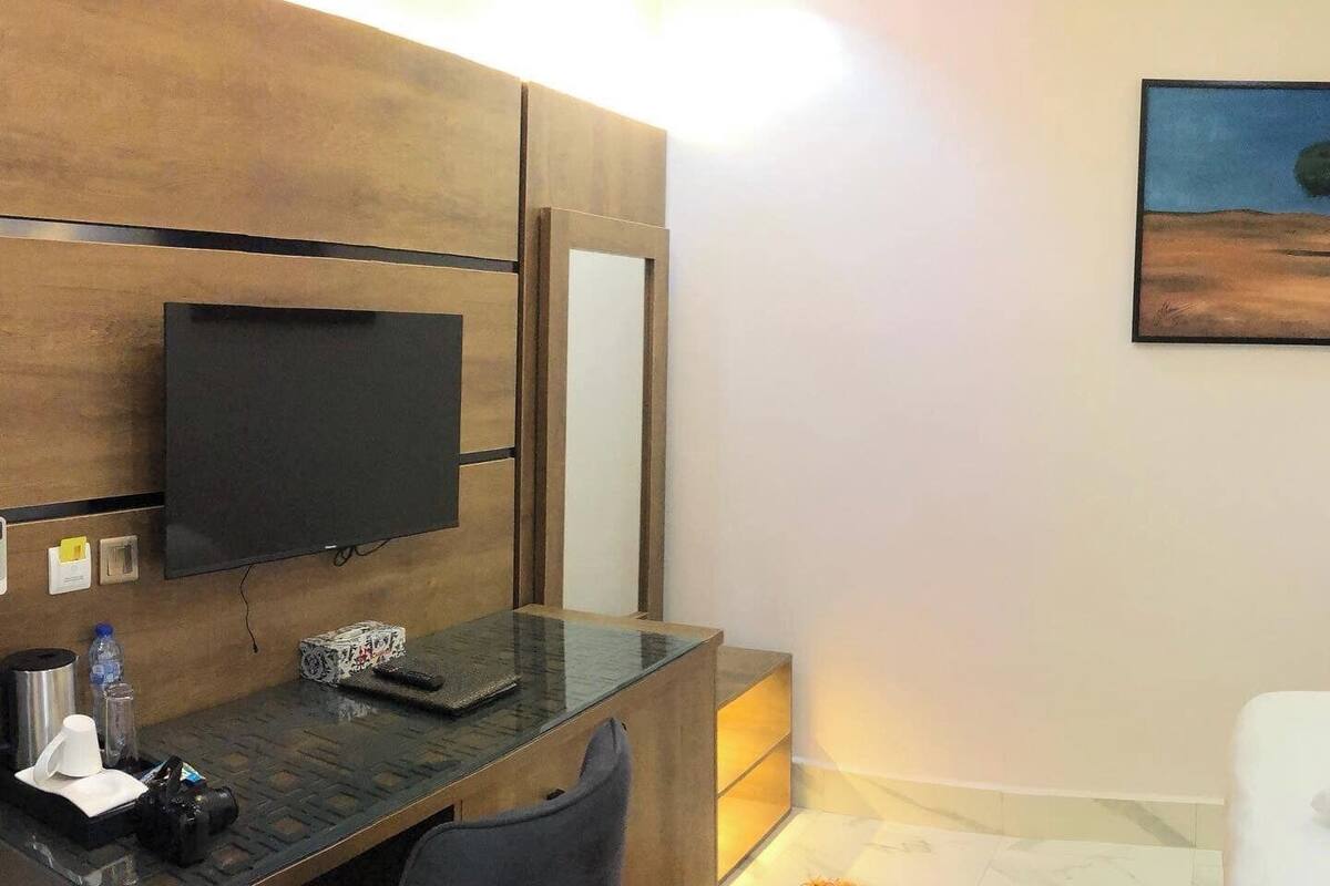 Moderni hotellihuone, jossa on puinen työpöytä, litteänäyttöinen televisio, peili ja ruskea matto.