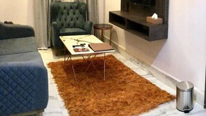 Ein modernes Wohnzimmer mit einem gepolsterten Sessel, einer Couch, einem Couchtisch und einem an der Wand befestigten Fernseher.