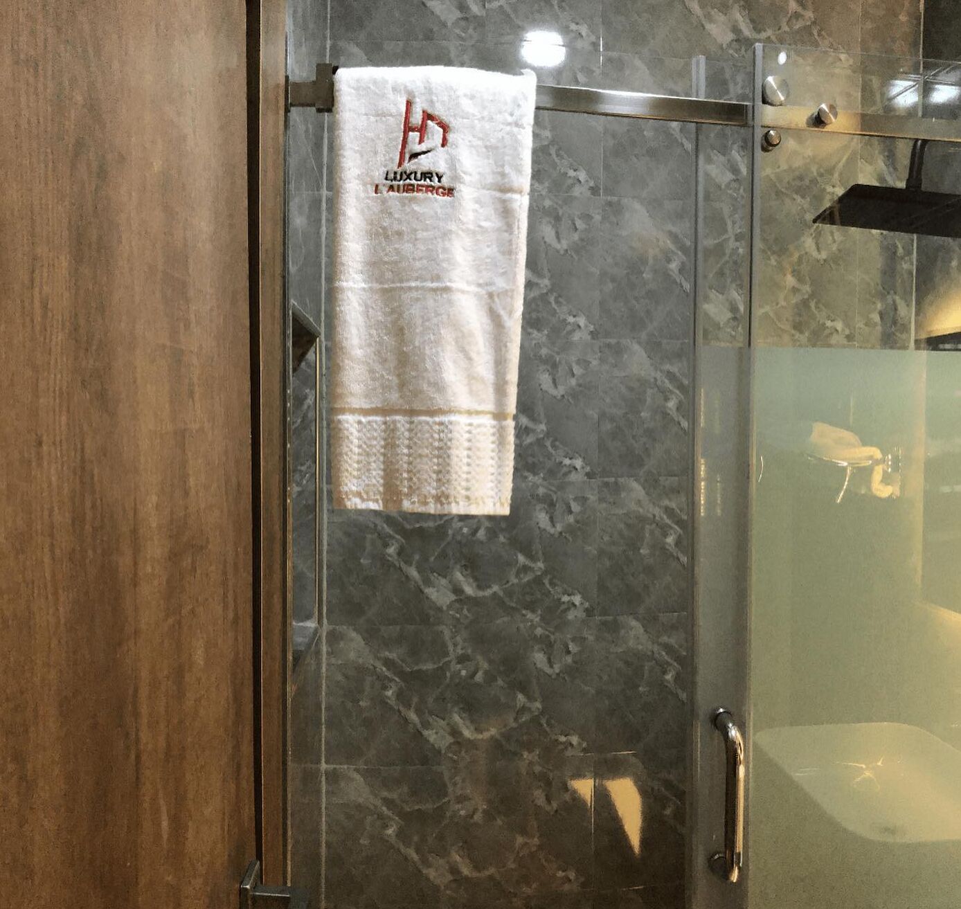 A glass shower enclosure with a white towel hanging on a metal bar, a wooden door, and a marble-like wall.