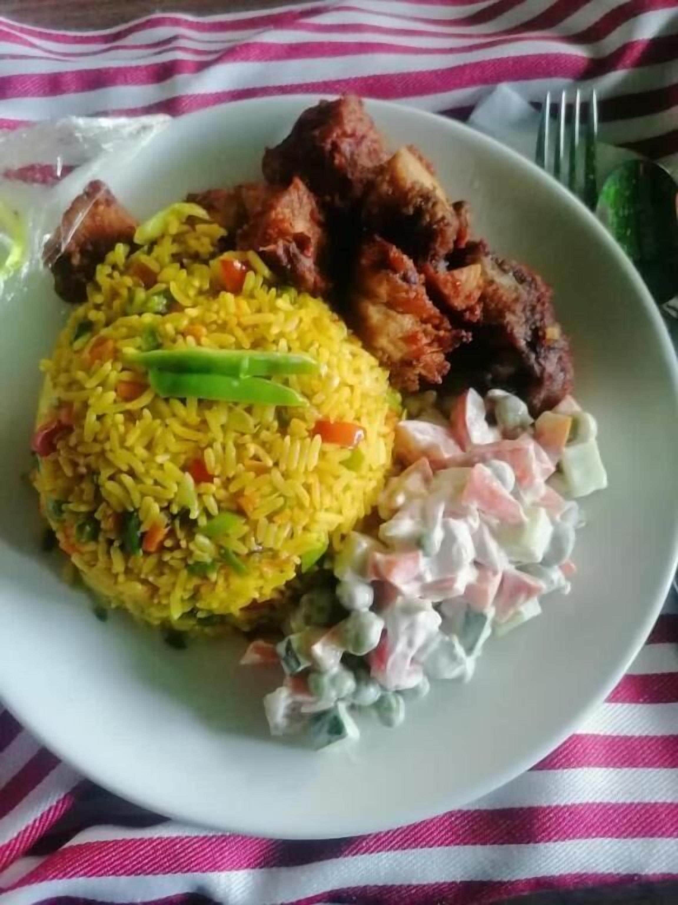 Un plato con arroz amarillo, carne frita y una guarnición de ensalada de col.