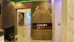 Ein Empfangsbereich mit einem Schild, auf dem 'LUXURY L'AUBERGE' steht, und einer Treppe im Hintergrund.