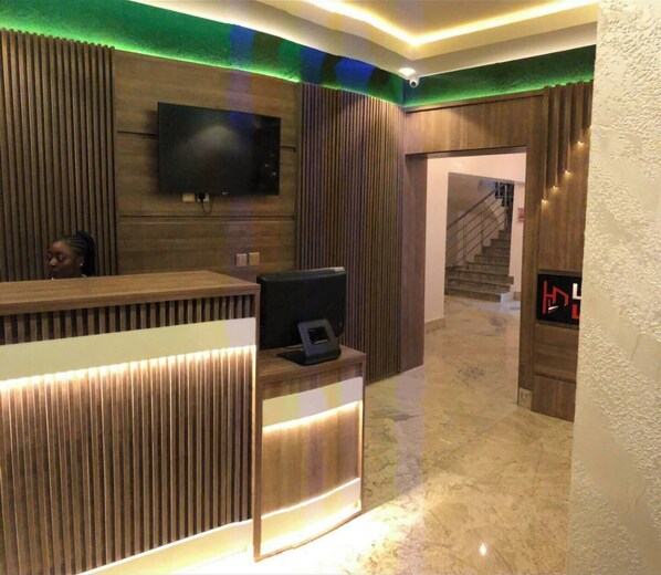 Un área de recepción con un mostrador de madera, un televisor de pantalla plana montado en la pared y una escalera que conduce a un piso superior.