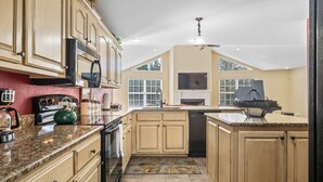 A kitchen with granite countertops, wooden cabinets, a microwave, a stove, and a ceiling fan.