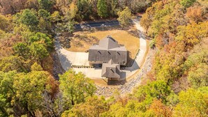 A large, two-story house with a central courtyard, surrounded by dense trees in autumn colors.