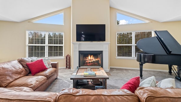 A living room with a fireplace, a black grand piano, a leather sofa, and a television mounted above the fireplace.