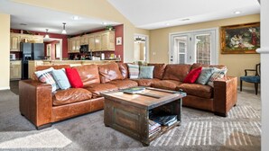 En rummelig stue med en stor, brun lædersofa, et sofabord og et køkken i baggrunden.