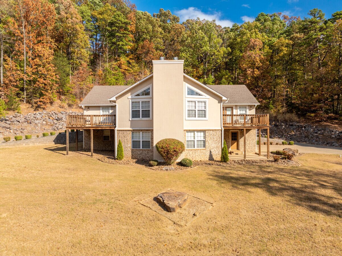 A two-story house with a balcony, a stone retaining wall, and a well-maintained lawn.