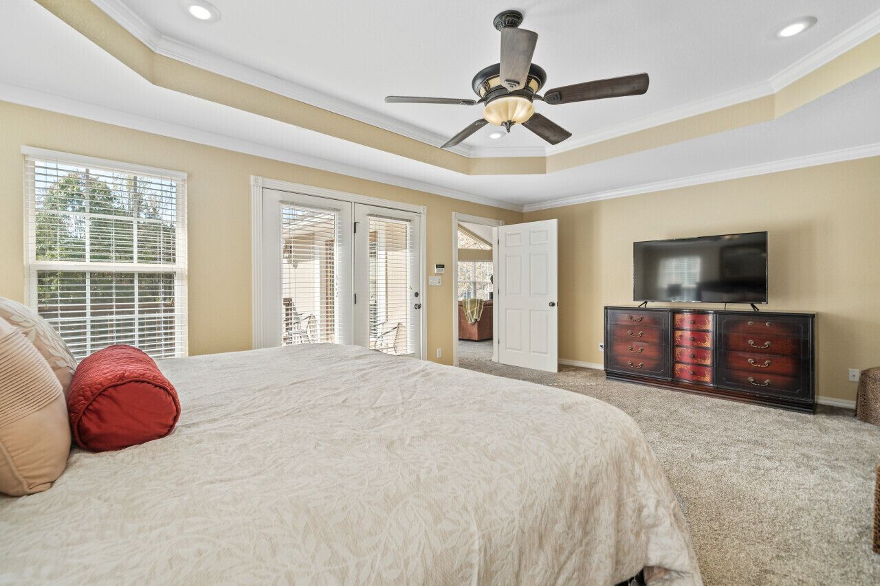 A bedroom with a large bed, a ceiling fan, a TV on a wooden cabinet, and a view of the outdoors through the sliding doors.