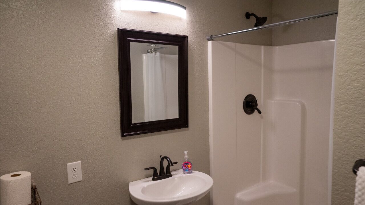 A bathroom with a white sink, a mirror, a shower, and a towel rack.