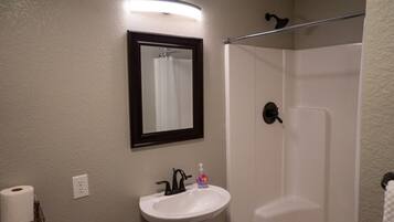 A bathroom with a white sink, a mirror, a shower, and a towel rack.