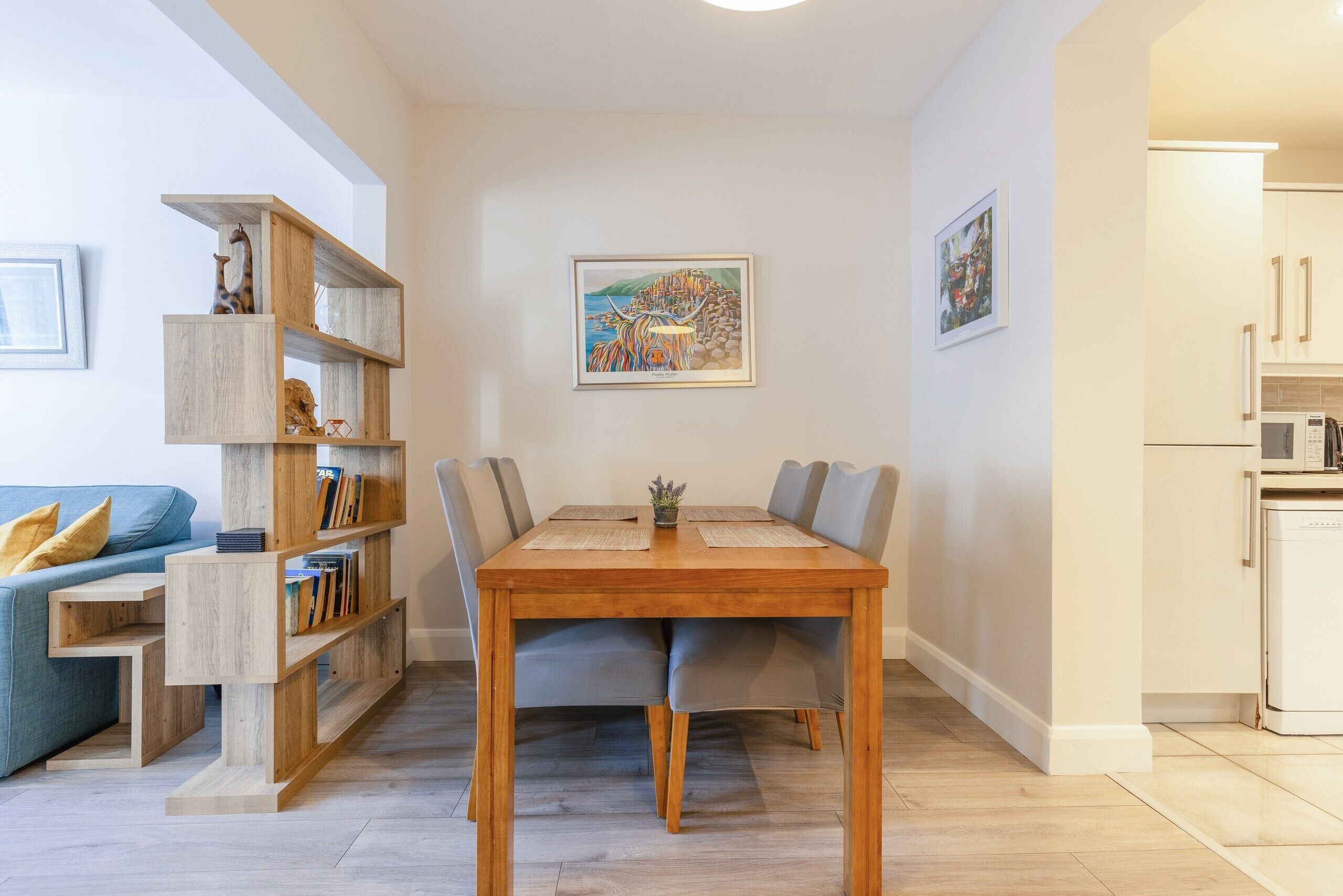 A dining area with a wooden table and chairs, a bookshelf, and a painting on the wall.