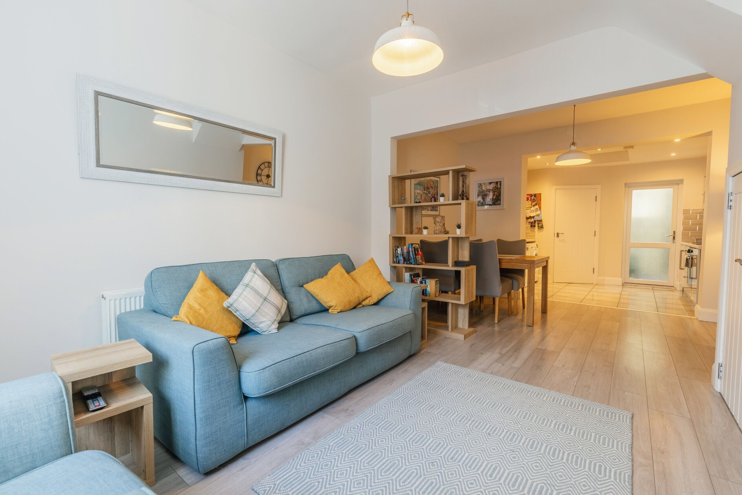 A modern living room with a blue sofa, a small side table, a patterned rug, and a bookshelf.