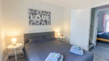 A neatly made bed with a grey headboard, two bedside tables with lamps, and a wall art piece with the word "LOVE".
