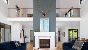 Un salón espacioso con chimenea, dos sofás azules, una mesa de centro y una alfombra grande.