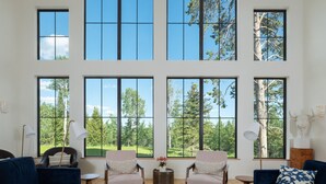 Amplia sala de estar con ventanas grandes, dos sofás, una mesa de centro y una lámpara.