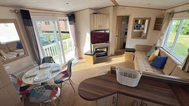 A caravan interior with a dining area, a sofa, a TV, and a kitchen area. - Burgh Castle 3-Bed Haven: Near Norfolk Broads (Burgh Castle)