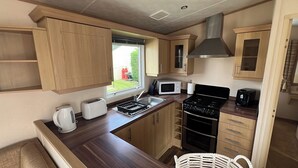 A compact kitchenette with wooden cabinets, a microwave, a stove, and a toaster. - Burgh Castle 3-Bed Haven: Near Norfolk Broads (Burgh Castle)