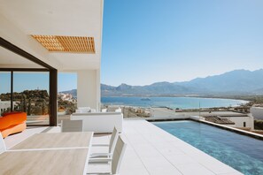 Un espace piscine extérieur moderne offrant une vue dégagée sur la mer et les montagnes.
