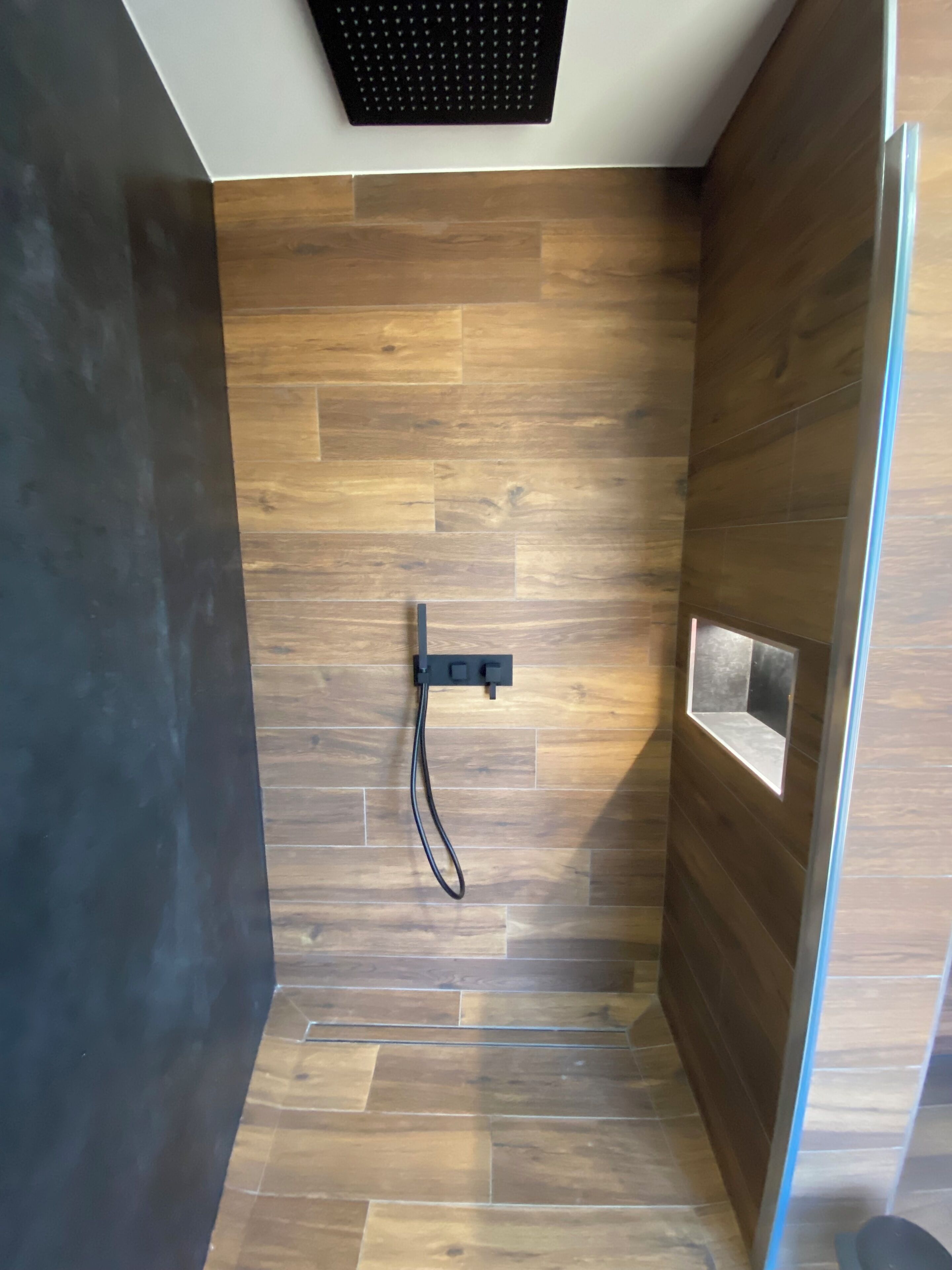 A modern shower area with wooden paneling and a black showerhead.