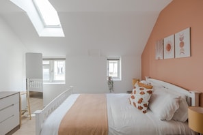 Relax in this serene bedroom with a large bed, bedside table, and dresser, offering views of the outside through two windows.