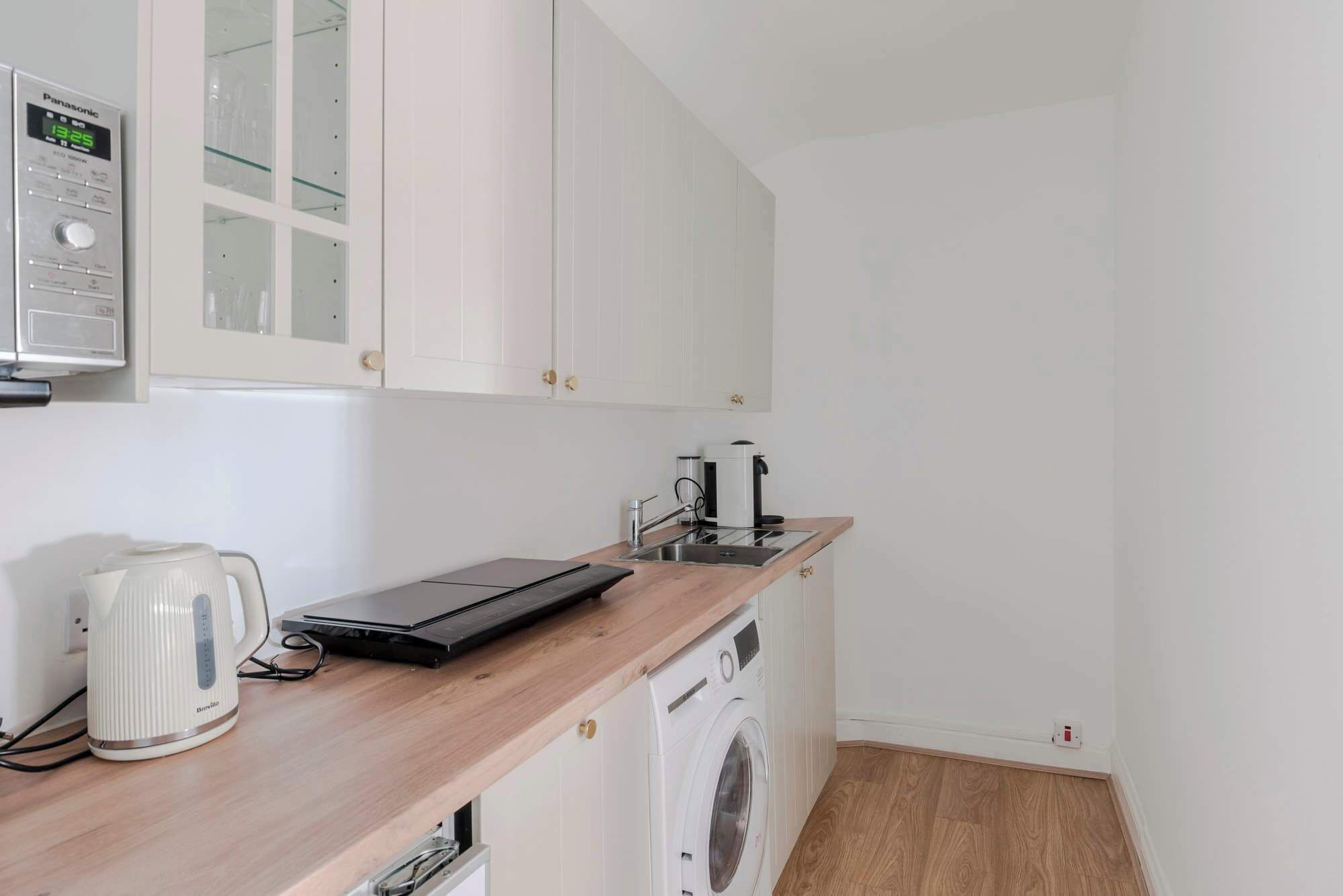 A compact kitchen with a microwave, kettle, coffee maker, and a washing machine.