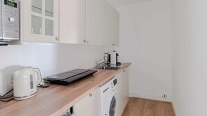 A compact kitchen with a microwave, kettle, coffee maker, and a washing machine. - Quiet Mews 1-Bed · Fitzrovia · Sleeps 4 (Greater London)