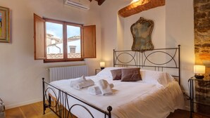 A bedroom with a bed, a window, a radiator, a stone wall, and a painting.