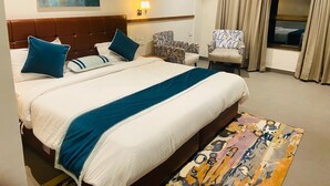 A hotel room with a large bed, two chairs, a window with curtains, and a painting on the wall. - Chokar Dhani Raipur (Raipur)
