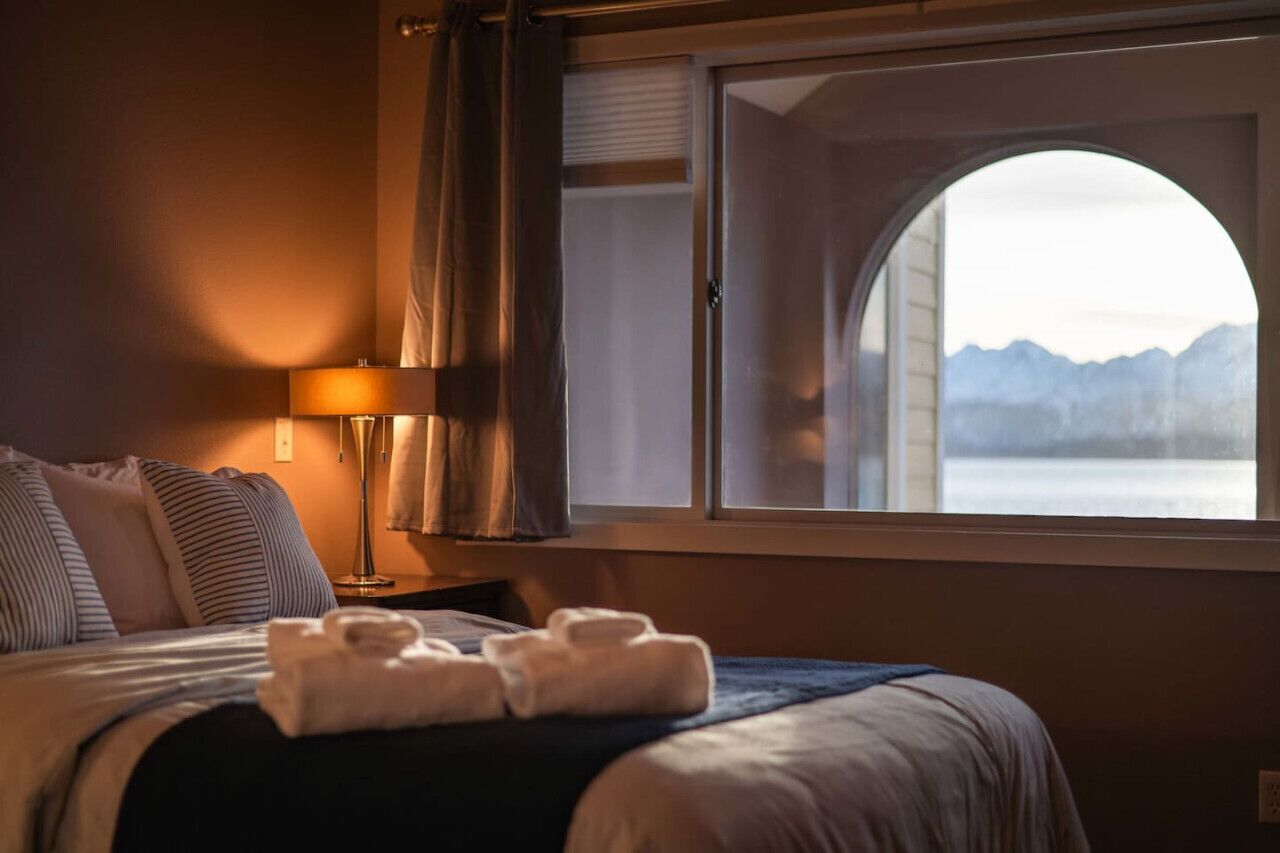 A hotel room with a bed, a nightstand with a lamp, a window with a view of mountains, and towels on the bed.